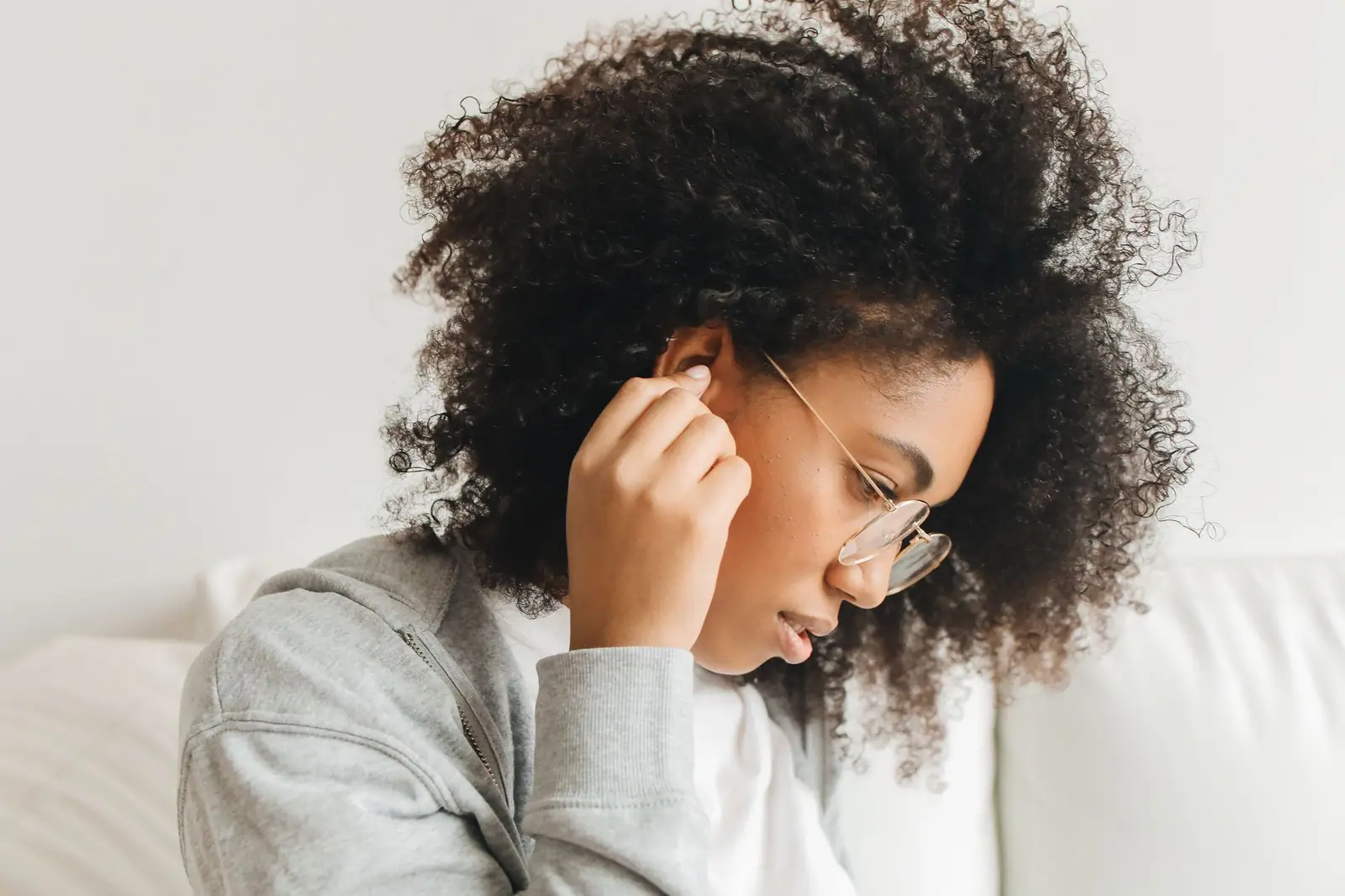 Woman in glasses touching her ear, thinking about hearing aids