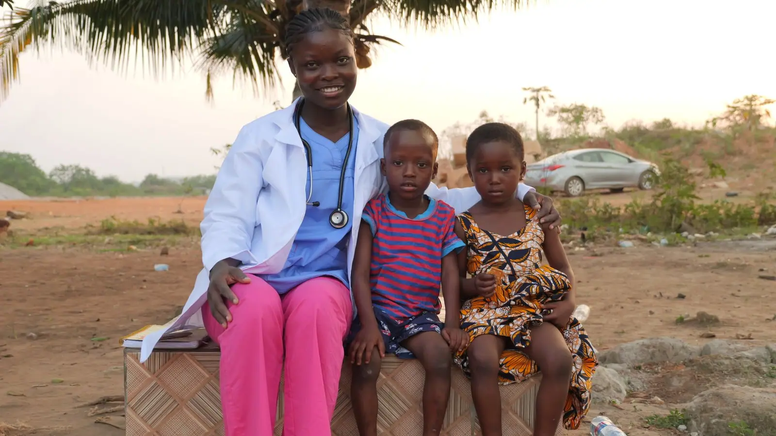 Health worker sitting with two children outdoors
